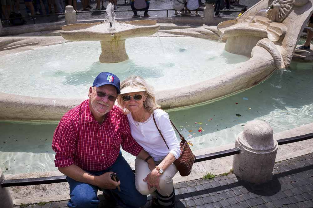 Tourist couple sitting down on the barcaccia water fountain at the Spanish steps